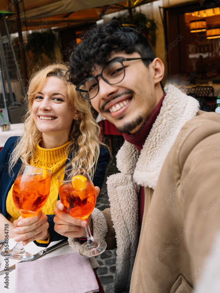Young multi-ethnic smiling couple taking a selfie while sitting in a restaurant having a drink selective focus