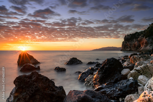 colorful sunrise at Cala Gonone with black and white rocks and boulders and a sunburst