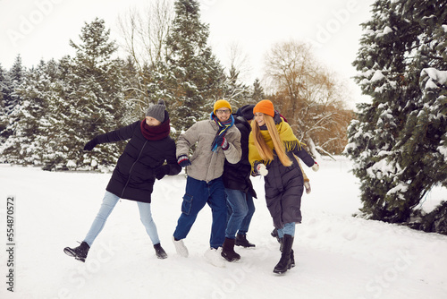 Group of cheerful active millennial friends in warm clothes walking in a winter forest. Happy young people gather in the park together, have fun and enjoy outdoor activities