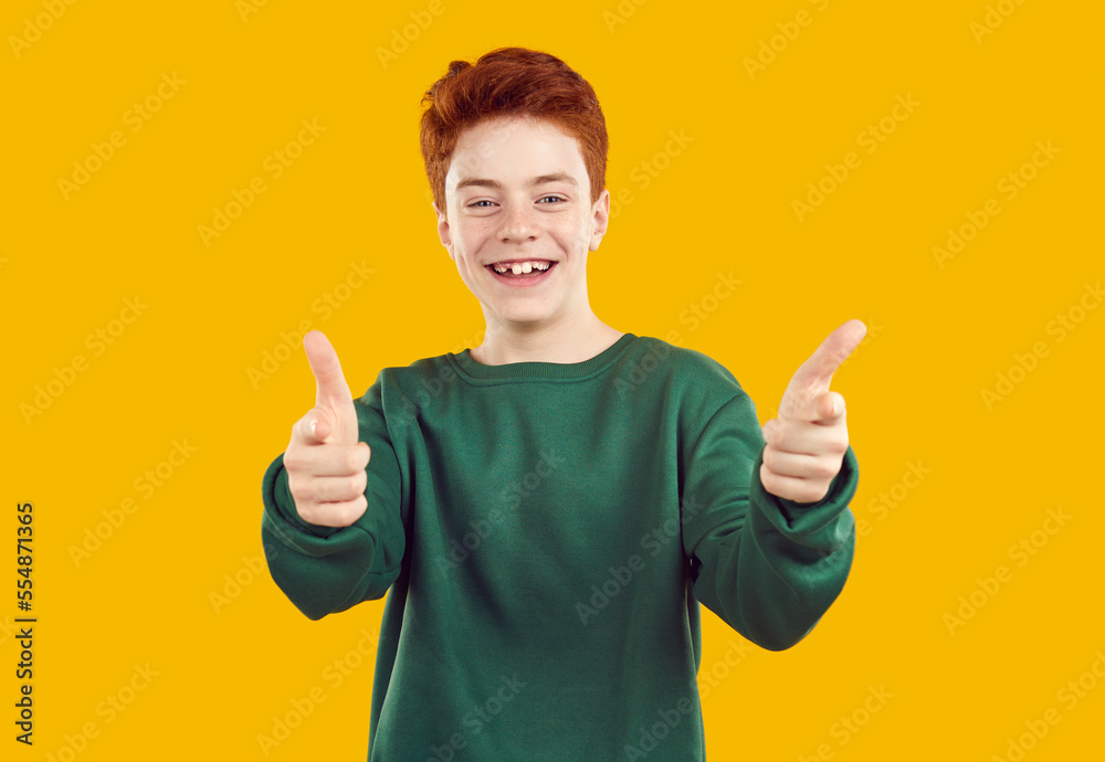 Portrait of happy, toothless, red-haired confident teenager in casual, warm, green sweater, looking and pointing fingers directly at you in the camera on an isolated yellow background. Portrait of happy, toothless, red-haired confident teenager in casual, warm, green sweater, looking and pointing fingers directly at you in the camera on an isolated yellow background.