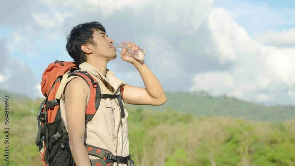 Young Asian man backpacker traveling in the forest. Male traveler holds a bottle of water. Healthy hiker drinking water in nature hike. Young man living active life, fun and smile. Young Asian man backpacker traveling in the forest. Male traveler holds a bottle of water. Healthy hiker drinking water in nature hike. Young man living active life, fun and smile.