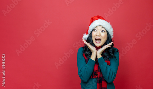 Pretty smiling asian woman in warm christmas sweater and santa hat is having excitement on red background for season celebration concept