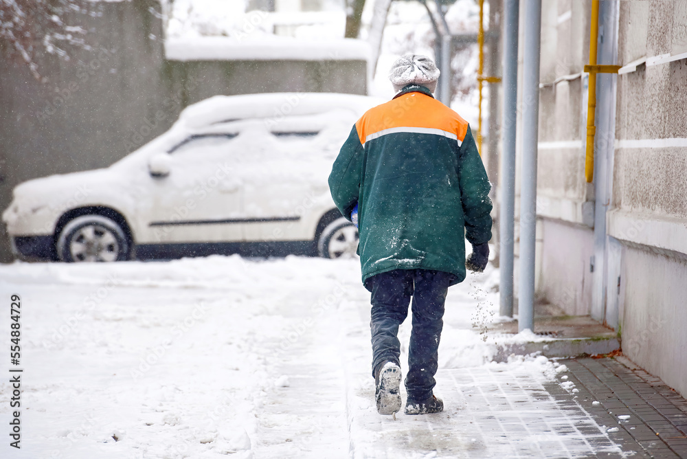 Worker with salt bucket spread salt mixture on walkway near residential building. Janitor melt snow spreading melting reagents, prevent slipping on road after snowfall. Janitor spread sand Worker with salt bucket spread salt mixture on walkway near residential building. Janitor melt snow spreading melting reagents, prevent slipping on road after snowfall. Janitor spread sand