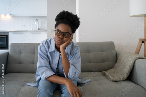Fotografija Tired exhausted African American woman sits on sofa in living room leaning on arm and looking into distance