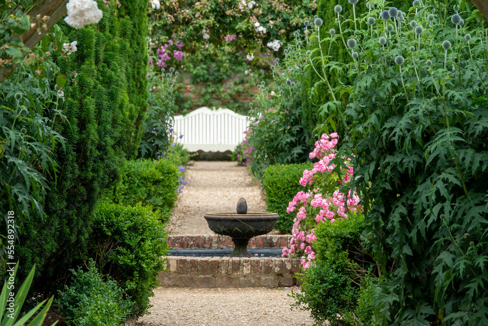 looking down a pathway through summer flowers to a fountain and a bench looking down a pathway through summer flowers to a fountain and a bench