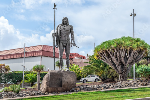 San Cristobal de La Laguna, Spain - November 24, 2021: Monument to Mencey Bencomo near the Dracaena draco in La Laguna town. Sculpture of a famous missionary with a staff and weapon on a city street