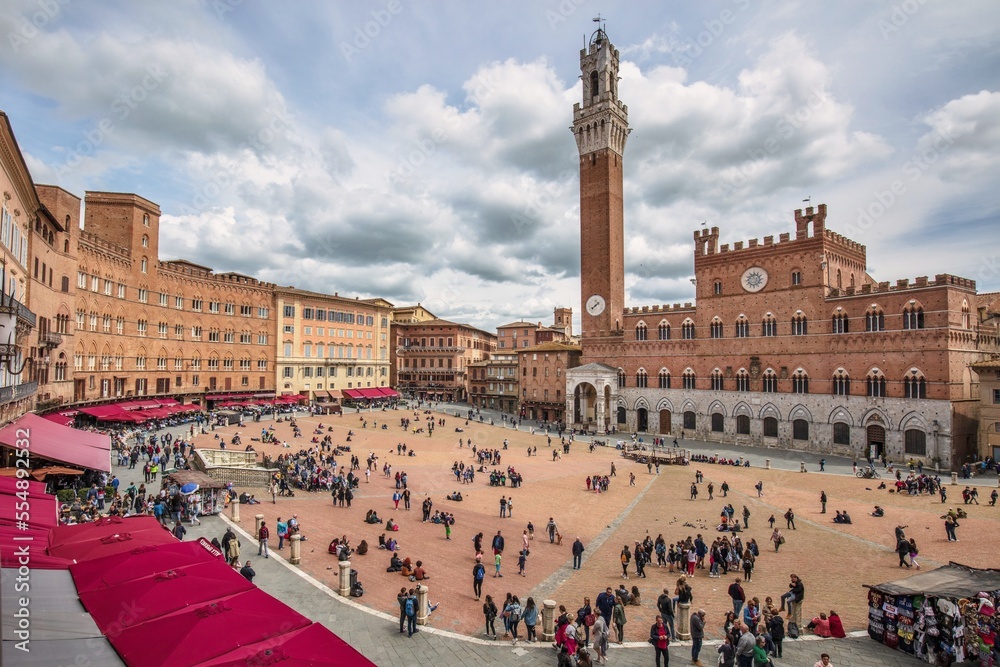 Piazza del Campo in Siena, Italy,
plaza among old typical colorful buildings and tall belfry on background under beautiful cloudy sky at evening