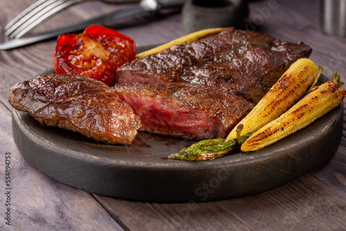 Roasted Top Blade beef steak with grilled vegetables in wooden plate.