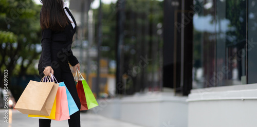 Young beautiful Asian woman holding colorful shopping bags walking on a city street. Happy woman with shopping bags enjoying in shopping. Consumerism, lifestyle city concept.