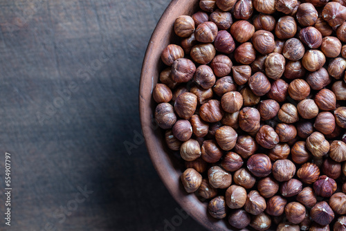 Dry hazelnuts in a ceramic plate on a wooden background. Heap of peeled hazelnuts kernels, top view, copy space for text