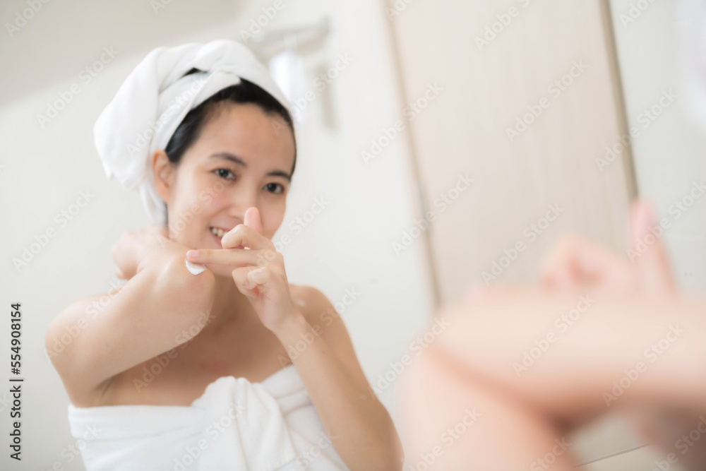 Happy young Asian woman applying lotions on her body in bathroom Happy young Asian woman applying lotions on her body in bathroom