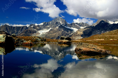 A landscape with a smooth Riffelsee lake surface and mountains and clouds reflected in it, on a mountain Gornergrat, near Zermatt, in southern Switzerland