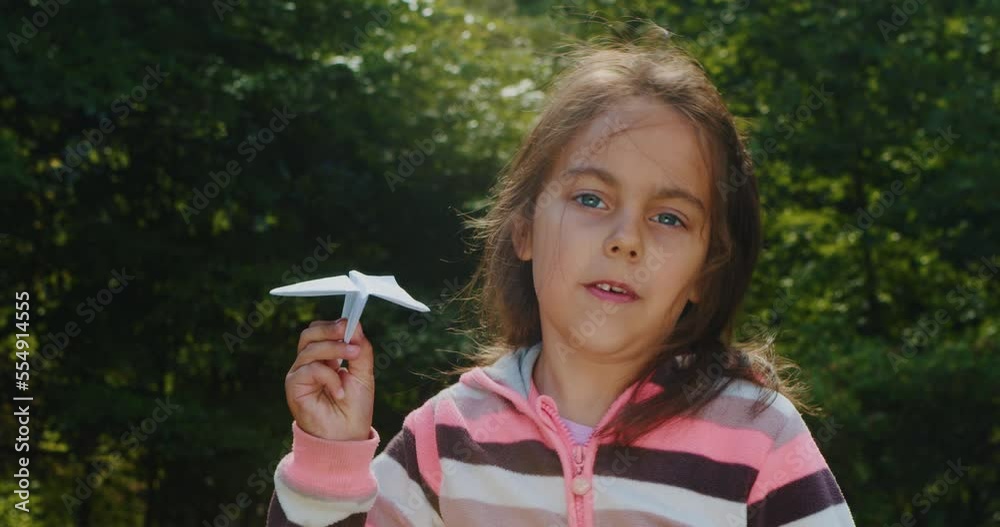 Cheerful little girl plays with a paper airplane in the forest in ...