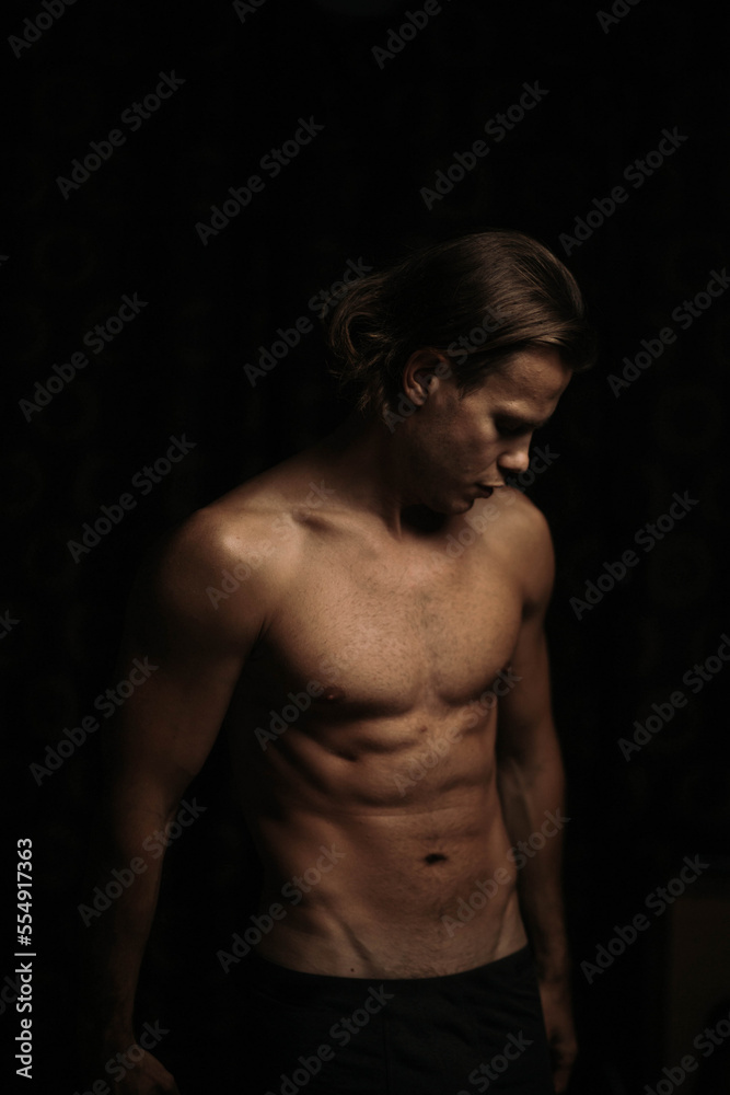 Naklejka premium man with an athletic body with a naked torso in the dark, a thin, athletic figure of a man.