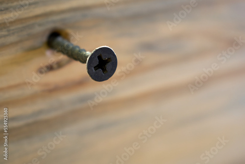A black self-tapping screw screwed into a wooden surface with the main focus on the head of the self-tapping screw
