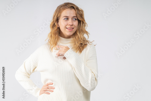 A young blonde girl with curly hair in a white knitted suit admires and poses on a white background