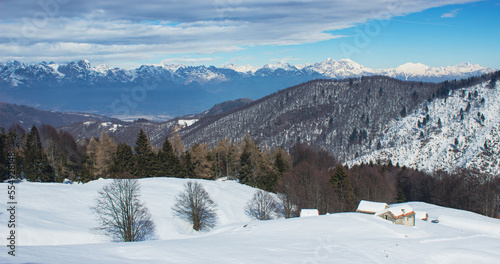 Postcard panoramic landscape. Small stone houses amid snowdrifts with mountains in the background. Photographed in Combai, Treviso, Italy. © JulyLo.Studio