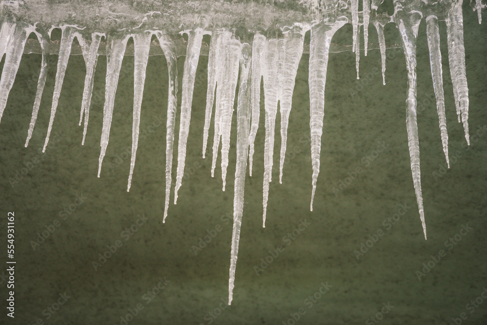 Icicles hanging from the roof on plaster wall background. Natural icicles of different sizes