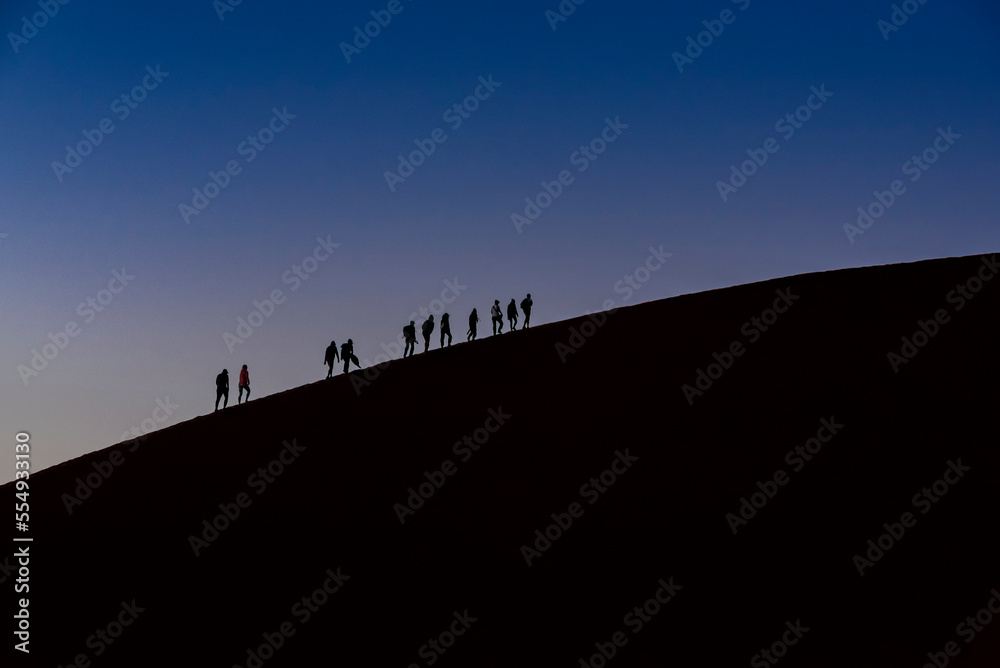 Silhouette of tourists climbing Dune 45 at dusk, Sossusvlei, Namib Desert; Namibia Silhouette of tourists climbing Dune 45 at dusk, Sossusvlei, Namib Desert; Namibia
