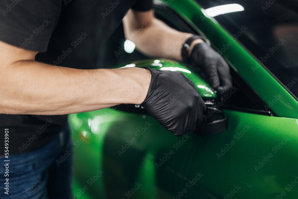 A man makes a detailing of a new car in good lighting, wrapping it with a transparent protection film A man makes a detailing of a new car in good lighting, wrapping it with a transparent protection film