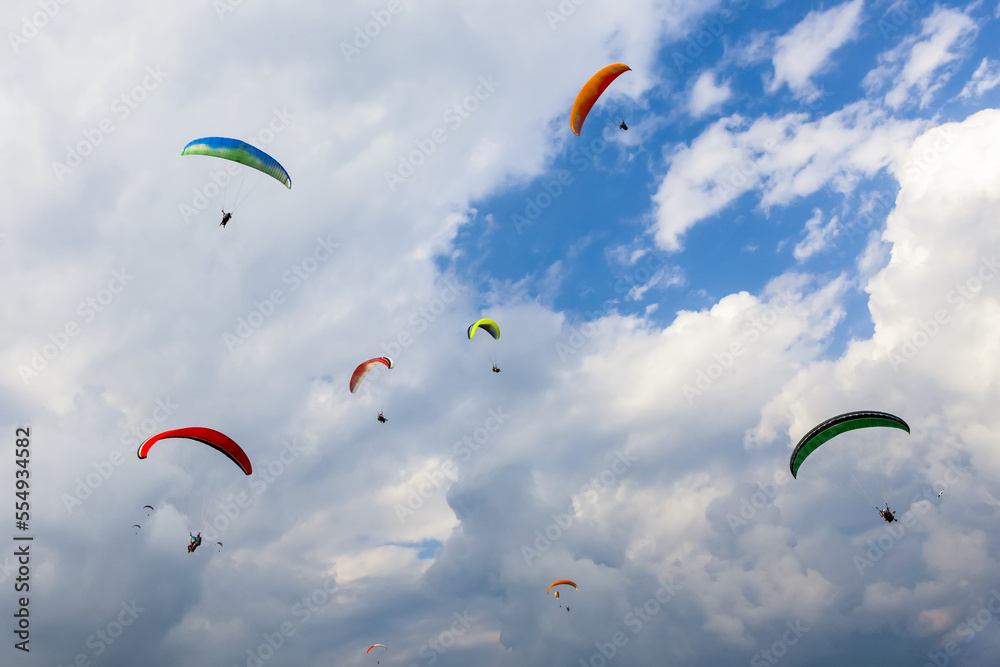 A group of colorful paragliders playing in the thermals above Sarangkot and the city of Pokhara on a sunny autumn day with a cloudy sky; Kaski District, Nepal A group of colorful paragliders playing in the thermals above Sarangkot and the city of Pokhara on a sunny autumn day with a cloudy sky; Kaski District, Nepal