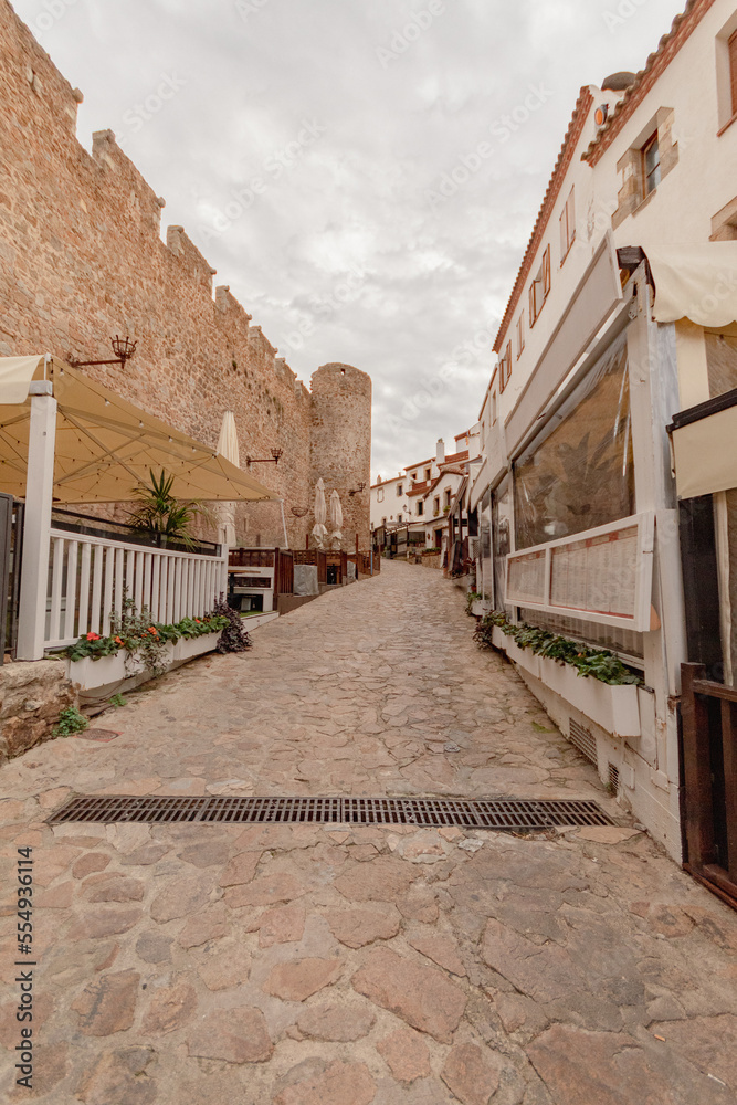 Antigua calle a las afueras de la muralla del castillo de Vila Vella en Tossa de Mar con un panorama frances con las terrazas de los restaurantes a los lados.