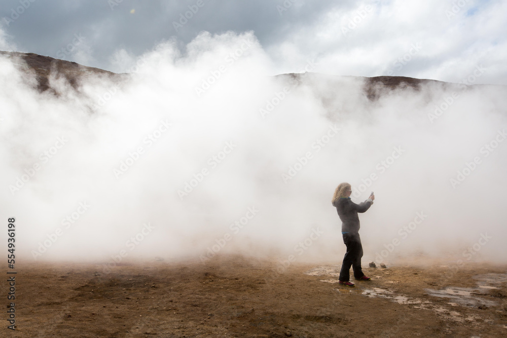 A woman photographs among the steaming mud pots geothermal area near Lake Myvatn.; Iceland A woman photographs among the steaming mud pots geothermal area near Lake Myvatn.; Iceland