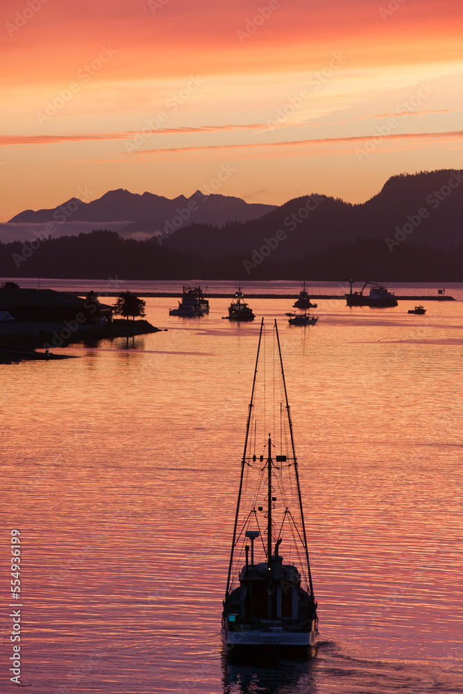 Under colorful skies at sunset, a boat carves the water near mountains, a marina and harbor.; Sitka, Alaska Under colorful skies at sunset, a boat carves the water near mountains, a marina and harbor.; Sitka, Alaska