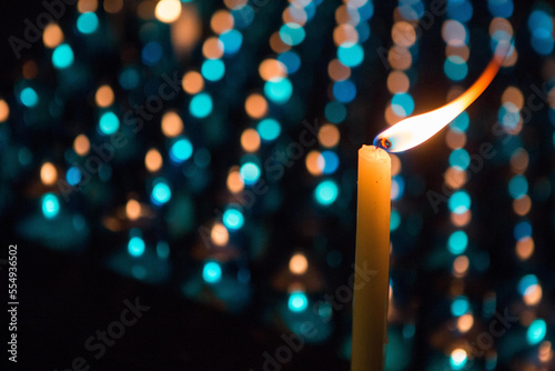 A candle with flame in front of rows of other candles.; Chartres, France photo