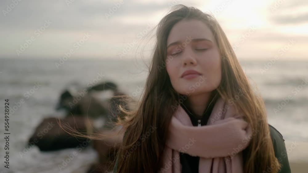 Pretty girl with closed eyes, dreaming on sea shore. Woman full of wonder relaxes standing on ocean coast during storm. Waves breaking on stone breakwater. Wind blows hair. Dreamy cinematic footage. Pretty girl with closed eyes, dreaming on sea shore. Woman full of wonder relaxes standing on ocean coast during storm. Waves breaking on stone breakwater. Wind blows hair. Dreamy cinematic footage.