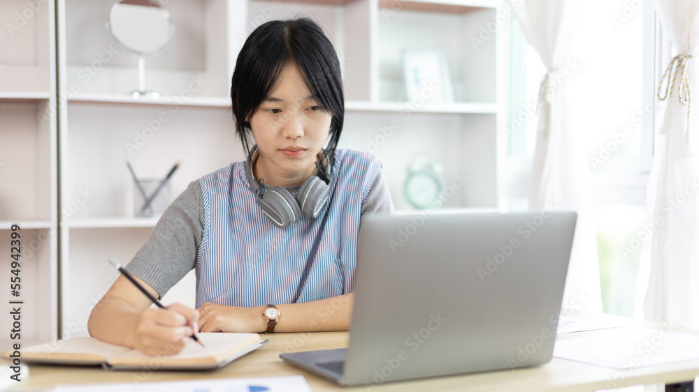 Asian woman taking notes in notebook while studying online in laptop at home, Video chat, Online communication , Stay home, New normal, Distance learning.., Social distancing, Learn online... Asian woman taking notes in notebook while studying online in laptop at home, Video chat, Online communication , Stay home, New normal, Distance learning.., Social distancing, Learn online...