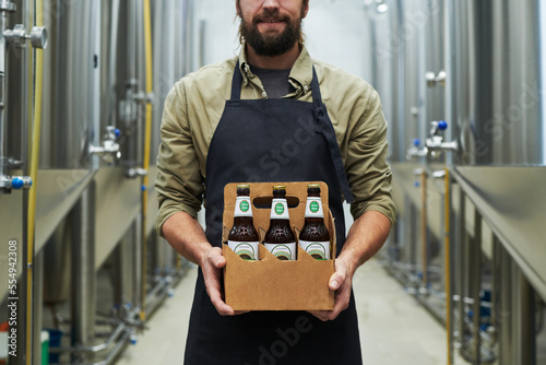 Obraz na plátně Cropped image of smiling brewer showing bottled beer produced in his brewery