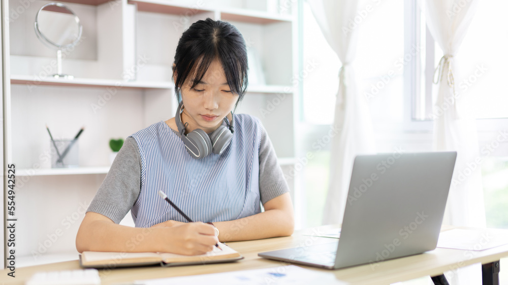 Asian woman taking notes in notebook while studying online in laptop at home, Video chat, Online communication , Stay home, New normal, Distance learning.., Social distancing, Learn online... Asian woman taking notes in notebook while studying online in laptop at home, Video chat, Online communication , Stay home, New normal, Distance learning.., Social distancing, Learn online...