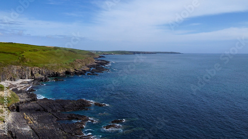 Green hills on the Atlantic Ocean on a sunny spring day. Blue sky over the sea coast. The coastline of Ireland  West Cork. Aerial photo. Drone point of view.