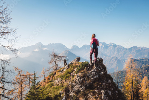 One lonely woman hiker standing in top of the rock looking at the breathtaking view of the mountains
