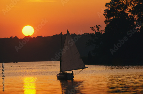 Gaff-rigged catboat sails along the shoreline at sunset.; Chesapeake Bay, Maryland. photo