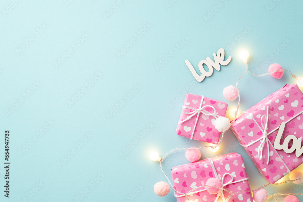 Valentine's Day concept. Top view photo of present boxes in wrapping paper with heart pattern light bulb garland inscriptions love and soft pompons on isolated pastel blue background with copyspace