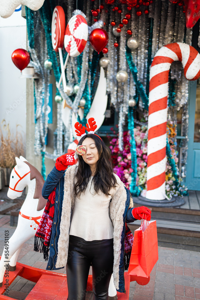 Attractive Asian girl with gift bag in her hands posing on a festive city street decorated for Christmas