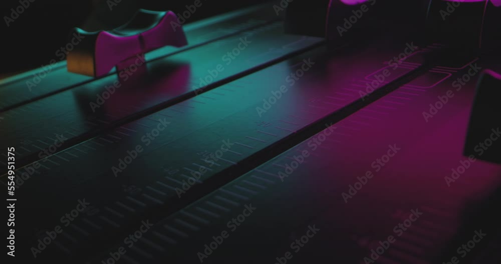 Close-Up Finger pushes audio mixer fader to max volume in colorful party lights