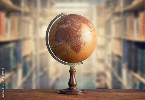 Old geographical globe and old book in cabinet with bookselfs. Science  education  travel background. History and geography team. Ancience  antique globe on the background of books.