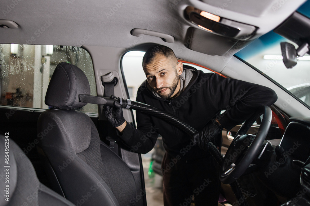 Obraz premium Details of car vacuum cleaning. Professional young male worker using vacuum cleaner for dirty car interior. Auto car service worker using vacuum cleaner to wash car seat.