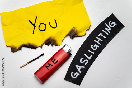 Word Gaslighting, on a black surface, next to a lighter with the word Me, and burnt yellow card with the writing You. Psychological meaning.