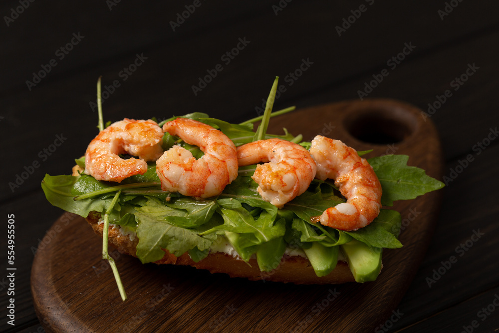 Bruschetta on a fresh baguette with arugula, cream cheese, avocado and shrimp on a wooden board Bruschetta on a fresh baguette with arugula, cream cheese, avocado and shrimp on a wooden board