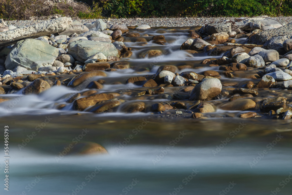 Obraz premium Water flowing over rocks, flowing through rocks. Long exposure time. A long exposition of the river in the Caucasus mountains. The stones in the river are blurred from long exposure.