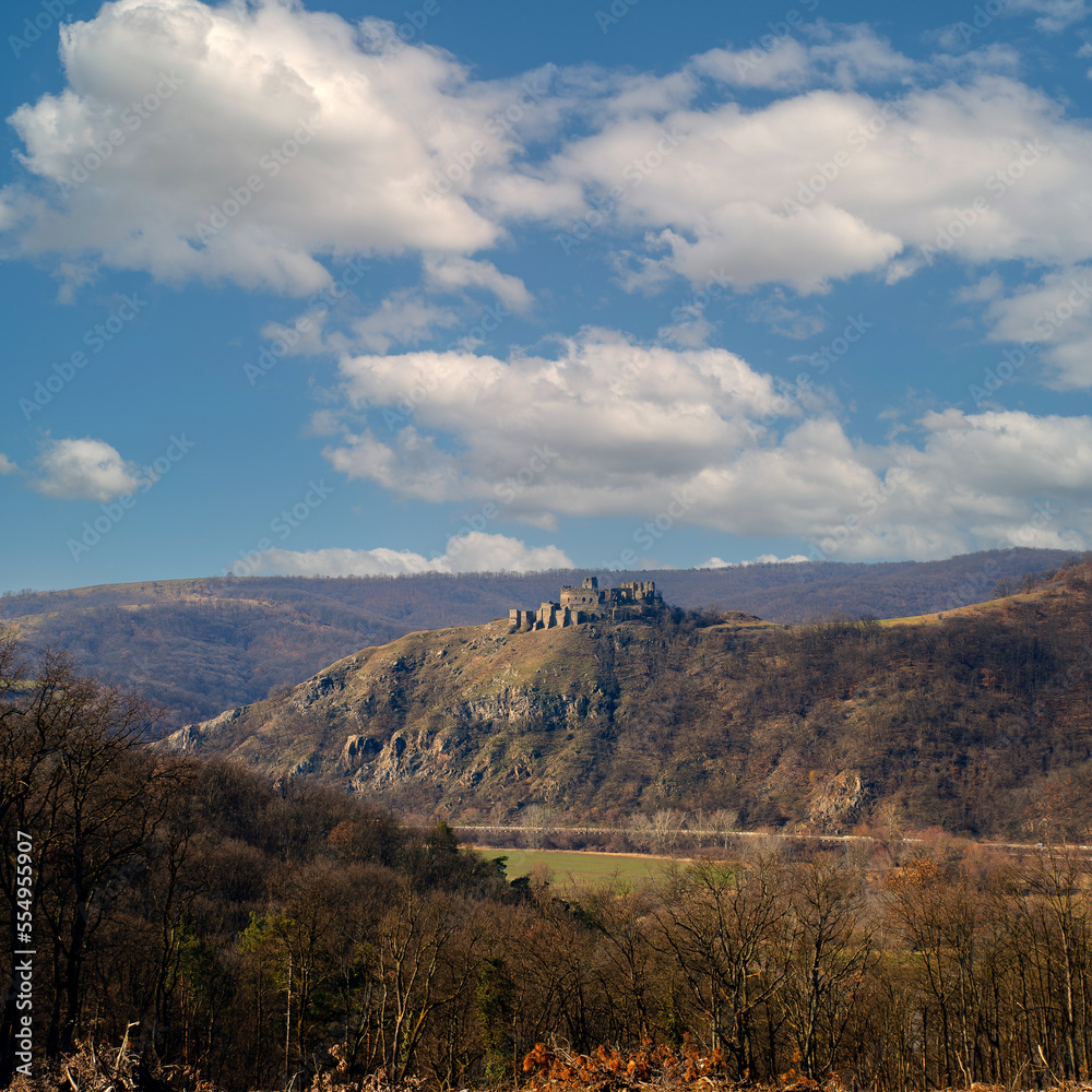 Medieval fortress on the hill of the mountain. Ruins of an old castle against a blue sky with clouds. Scenic view of the fortress mountain landscape in late autumn