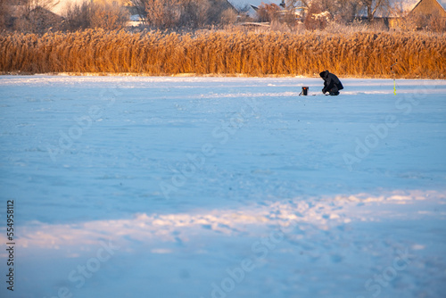 A fisherman on winter fishing on a frosty evening sits on an ice floe