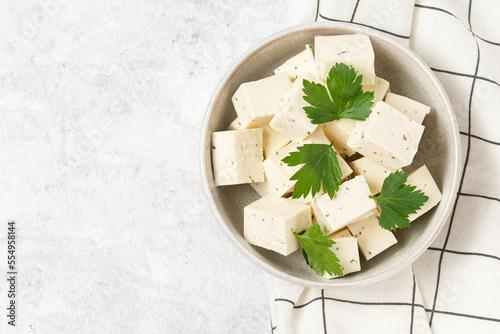 Tofu soy cheese or paneer or feta cheese cubes adding fresh parsley and celery in a ceramic bowl on a checkered napkin isolated top view