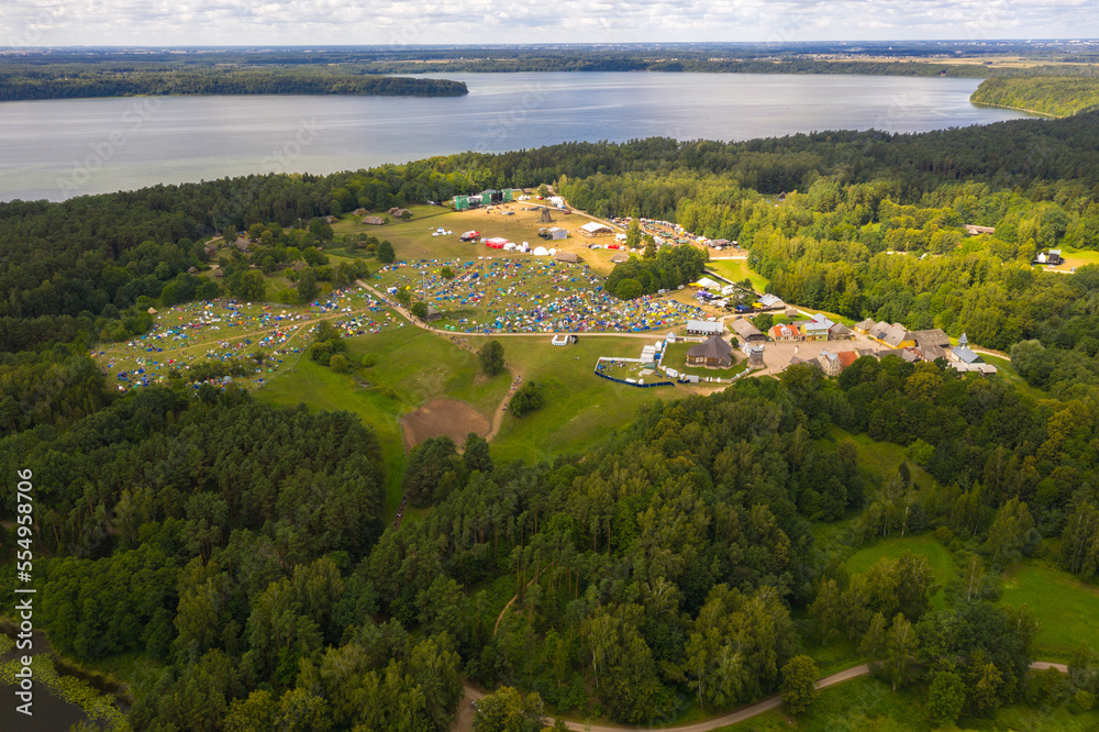 Drone view of music festival in a forest near a lake during summer