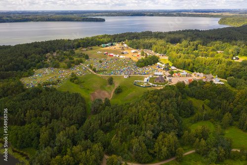 Drone view of music festival in a forest near a lake during summer