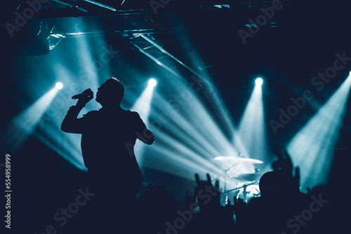 Rock singer on scene in club. Bright stage lighting. Band Blue Silhouette. Vocalist singing to microphone. hand fans during a concert